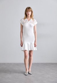 Abito bianco lavorato a maglia con orlo svasato, caratterizzato da un design perforato sulle spalle e sul colletto. Texture liscia, maniche corte, lungo fino al ginocchio.