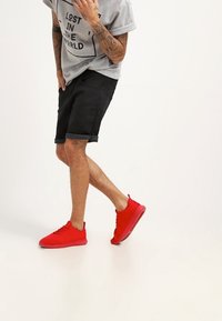 Zapatillas deportivas rojas con una textura suave y un diseño minimalista. Combínalas con pantalones cortos negros y una camiseta gráfica de color gris claro.