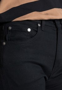 Black denim jeans featuring a slim fit, classic five-pocket design, and silver hardware on the front pockets. Smooth texture and no visible patterns.
