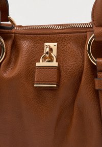 Brązowa skórzana torebka z ozdobą w postaci złotego zamka, zamknięciem na zamek i teksturowaną powierzchnią. Dodatki to złote okucia i okrągłe pierścienie.