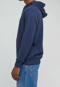 Sudadera azul marino con bolsillo frontal tipo bolsa, puños y dobladillo acanalados, y capucha con cordón ajustable. Material suave y corte relajado.