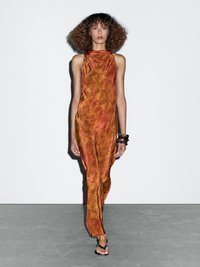 Robe en soie orange brûlé avec un col haut, une silhouette décontractée et de subtils motifs floraux. Portée avec des sandales plates noires et des bracelets empilés.