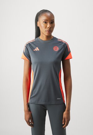 Grå idretts skjorte med oransje detaljer og sidepaneler. Har Adidas-logoen og et rundt Bayern München-bånd. Lett og pustende stoff.
