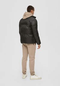 Schwarze Daunenjacke mit einer beigen Kapuze, mit gestepptem Design, glatter Textur und gerippten Bündchen. Kombiniert mit beigen Jogginghosen und weißen Sneakers.