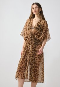 Kimono-tyylinen peite, jossa on leopardi-kuvio ruskeana ja beigeinä, kevyt läpikuultava kangas, avoin etuosa ja nyöriyksityiskohta vyötäröllä.