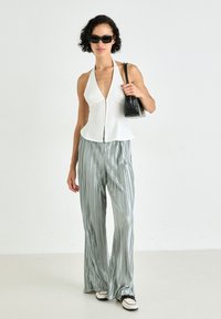 Top blanco sin mangas con un cuerpo ajustado, combinado con pantalones de pierna ancha plisados de color verde claro. Los accesorios incluyen gafas de sol negras y un bolso pequeño.