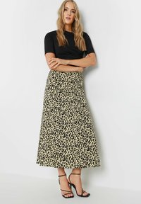 Jupe maxi à motif léopard en beige et noir avec une texture lisse, assortie à des talons hauts noirs à lanières.