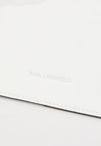 White leather wallet featuring embossed "KARL LAGERFELD" logo, neat stitching, and a smooth texture. Simple design with no additional accents.