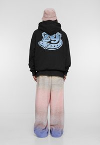 Sudadera negra con un diseño gráfico azul en la parte trasera, combinada con pantalones holgados de colores pastel que hacen un degradado de rosa a azul.