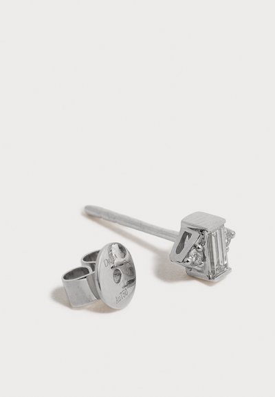 Boucle d'oreille clou en argent unique avec une pierre précieuse rectangulaire claire et un fermoir papillon avec des marquages gravés sur une surface blanche.