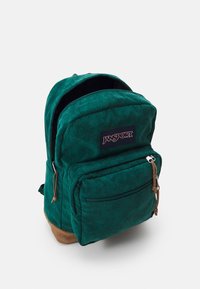 Green corduroy backpack with a front zip pocket, logo patch, tan bottom, and textured stripes. Features adjustable shoulder straps and a curved top.
