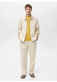 Beige linnen skjorta, gul T-shirt under, krämfärgade byxor, parat med svarta sandaler. Enkel design; inga synliga mönster eller hårdvara.