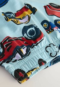 Elastisk talje shorts i lys blå stof med farverige lastbilmønstre. Har en sammensnøret kant og glat tekstur.