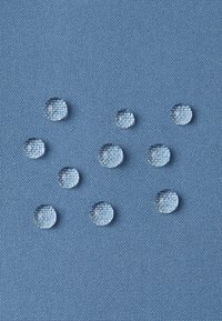 Tessuto blu con una superficie texturizzata, caratterizzato da diverse gocce d'acqua trasparenti sparse sopra. Le gocce sono rotonde e variano in dimensione.
