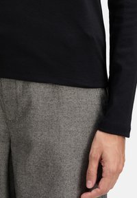 Maglietta nera a maniche lunghe con una consistenza liscia, abbinata a pantaloni grigi a motivo chevron, caratterizzati da una vestibilità ampia e colori neutri.