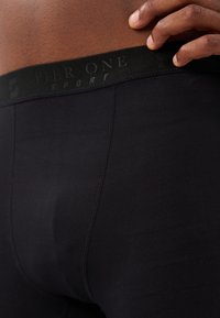 Juodi sportiniai šortai su tekstūruotu juosmeniu, ant kurio iškilmingai užrašyta "Pier One Sport". Audinys yra lygus, su prisitaikančia siluetu.