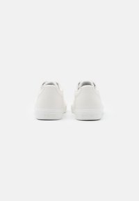 Sneakers bianchi in pelle con una finitura liscia, forma arrotondata e suola piatta in gomma. Marchio sul tallone e dettagli di design minimalisti.