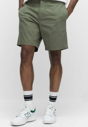 Olive green shorts made of cotton blend, featuring a flat front design, side pockets, and a straight cut, paired with white sneakers and striped socks.