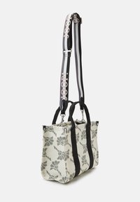 Sac en toile avec motif floral en gris clair et noir. Il possède des poignées supérieures doubles et une sangle amovible avec des détails de logo.