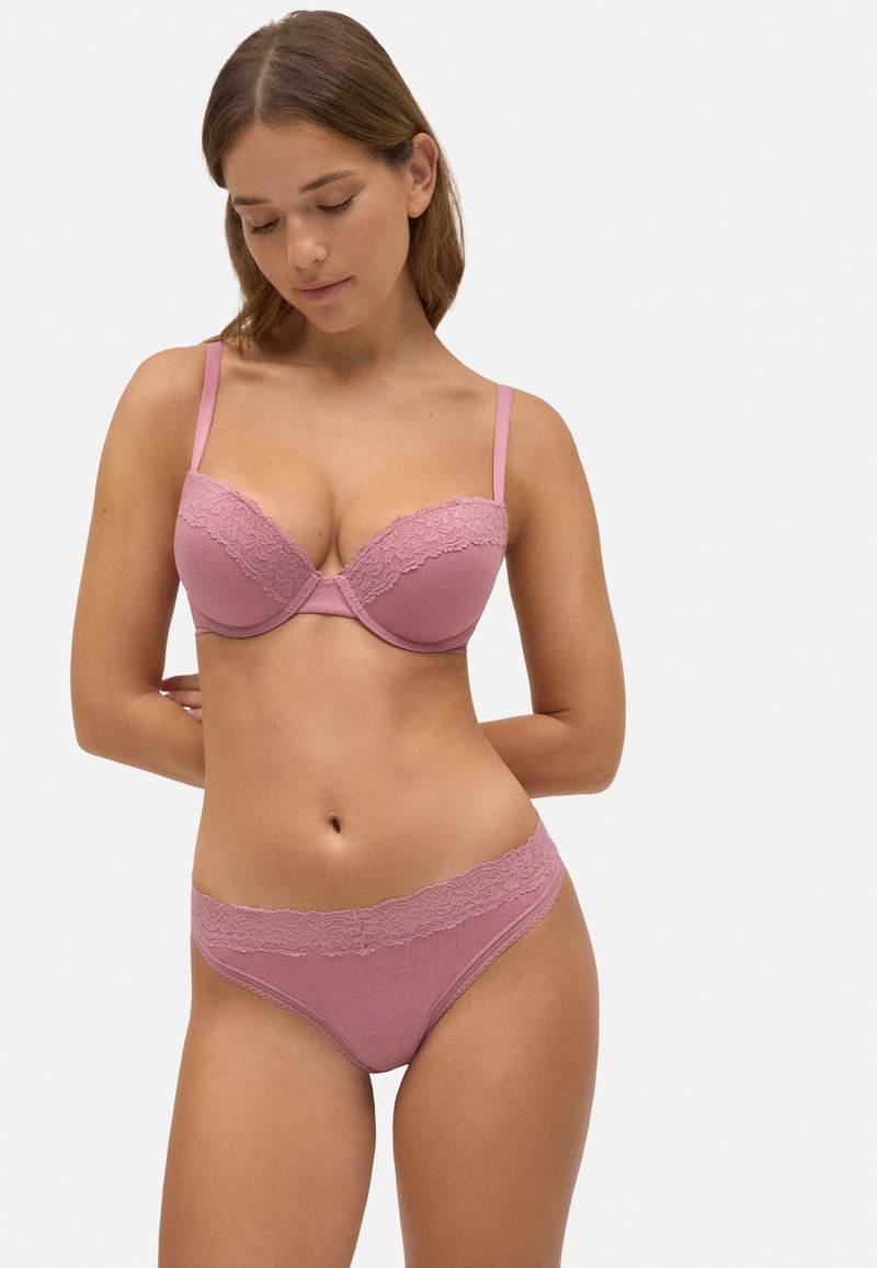 Conjunto de lencería en rosa claro que incluye un sujetador con realce y adorno de encaje, y unas braguitas de bikini a juego. Textura suave, tirantes ajustables y tejido acanalado.