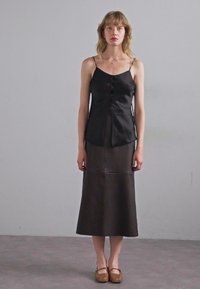 Svart silkespets med knappliknande detaljer, i kombination med en lång brun satinskirt med en smidig yta. Bärs med bruna vävda sandaler.
