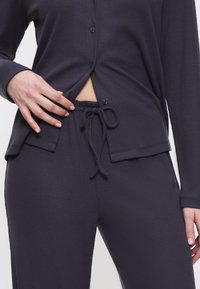 Donkergrijze lounge-outfit bestaande uit een geribbelde textuur, een lang mouwtop met knopen en een broek met trekkoord en een verstelbare taille.