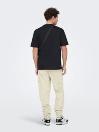 Sort bomulds-T-shirt med løs pasform, kombineret med lyse beige cargobukser med sidelommer. Sorte og hvide sneakers fuldender looket.