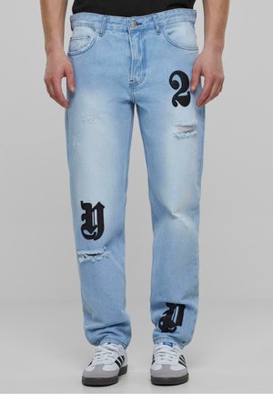 Světle modré džíny z denimu s odřeným vzhledem a černými grafickými čísly "2" a "Y" na přední straně. Klasický design s 5 kapsami.