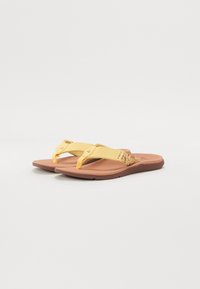 Flip-flops galbene cu curele texturate, ornamentate cu accente florale, o talpă plată de culoare maronie și un suport conturat pentru confort.