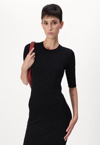 Abito knit nero con maniche corte e scollo rotondo, caratterizzato da un motivo sottile. Il modello tiene una borsa a spalla rossa.