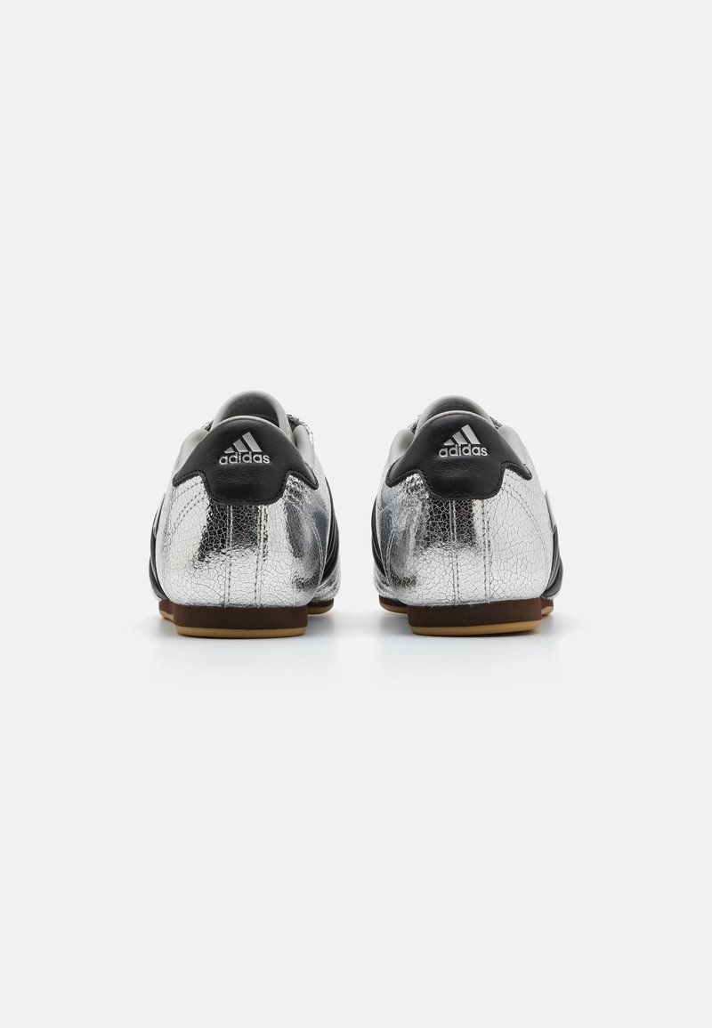 Las botas de fútbol negras y plateadas presentan un acabado metálico texturizado, un collar acolchado y una suela de goma que proporciona tracción. Marca Adidas en el talón.