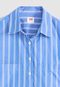Light blue striped button-up shirt featuring white vertical stripes, a pointed collar, two front pockets, and white buttons.
