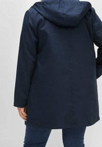 Waterdichte marineblauwe jas met een capuchon, voorzien van lange mouwen en een rechte snit. Gladde textuur met minimale naden.