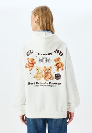 Crème-kleurige hoodie met grote teddybeerafbeeldingen op de achterkant, met tekst in bruin. Zachte stof, relaxed fit en met capuchon.