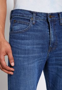 Vaqueros de mezclilla azul oscuro con corte recto, diseño de cinco bolsillos y costuras en contraste. La tela tiene una textura lisa y ligeramente desvanecida.