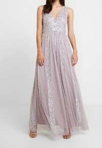 Maxikleid in Flieder mit V-Ausschnitt, verziert mit silbernen Pailletten und gepunkteten Details. Der fließende Stoff sorgt für einen eleganten Fall.