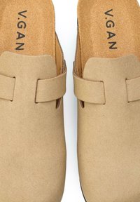 Beige vegan slip-on clogs with a smooth suede-like texture, featuring two wide straps and a contoured insole exhibiting the logo "V.GAN."