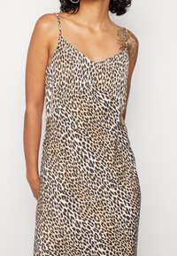 Robe caraco à imprimé léopard avec fines bretelles, présentant un design drapé et une texture douce, dans des tons beige, marron et blanc.