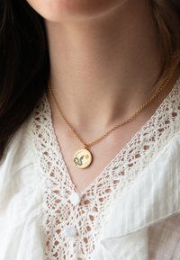 Gold necklace with a circular pendant featuring a black crescent and star design, displayed against a white lace blouse.