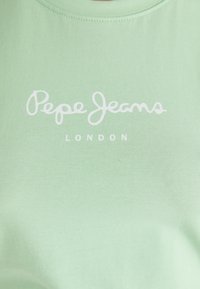 Minta vihreä puuvillapaita, jossa on valkoinen käsin kirjoitettu logo "Pepe Jeans" ja "LONDON" sen alla. Lyhyet hihansuut ja pyöreä kaula-aukko.