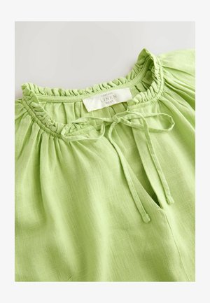 Jasnozielony lniany top z marszczonym dekoltem ozdobionym falbanką i wiązaniem, wykonany z teksturowanej, przewiewnej tkaniny.