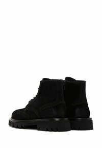 Botas de tobillo de ante negro con cordones en la parte delantera, costuras decorativas y suelas de goma gruesa con borde serrado.