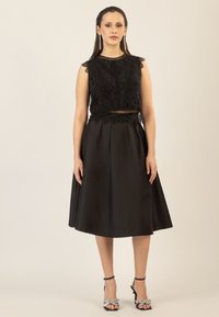 Vestido negro con un corsé de encaje y diseño sin mangas, falda en forma de A, acentos texturizados y combinado con tacones con tiras que presentan detalles decorativos.