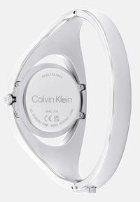 Montre-bracelet en acier inoxydable avec un boîtier élancé et courbé, une finition argentée brillante et une surface lisse. Détails de la marque et des spécifications gravés à l'arrière.