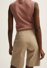 Úpletová bezrukávová halenka v jemně růžové, v kombinaci s béžovými šortkami na míru s zadními kapsami a hladkou texturou.