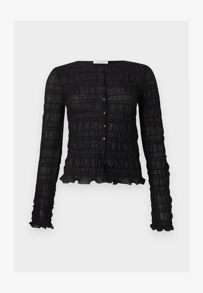 Mustast pika varrukaga nööbitav pluus, millel on tekstuuriga ruuduline muster ning volangidega ääred varrukate ja ääre juures.