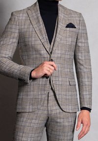 Completo a scacchi beige con righe blu. Vestibilità su misura, rever a punta, chiusura con un solo bottone, abbinato a un dolcevita nero sotto.