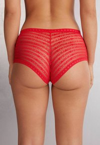 Rode kant boyshorts van doorschijnend gaas met een herhalend tekstpatroon. Golvende randen op de tailleband en beenopeningen. Achteraanzicht weergegeven.