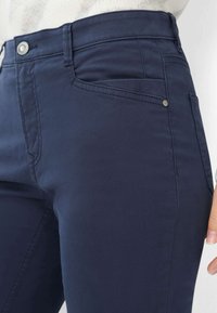 Pantaloni aderenti blu navy realizzati in tessuto di cotone liscio, con un classico design a cinque tasche e chiusura con bottone metallico in vita.