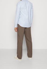Camisa azul claro de botones y mangas largas, combinada con pantalones marrones y zapatillas crema; tejido suave y corte relajado.